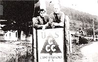Two unidentified enrollees of Camp Parsons at the entrance with some camp buildings in the background, From page 52,
